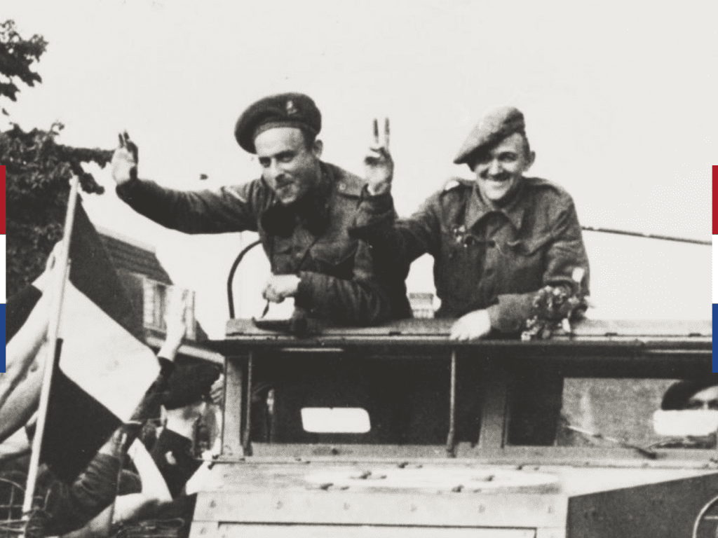 Zwart-witfoto van twee militairen die juichend uit een militair voertuig hangen terwijl mensen naar hen zwaaien