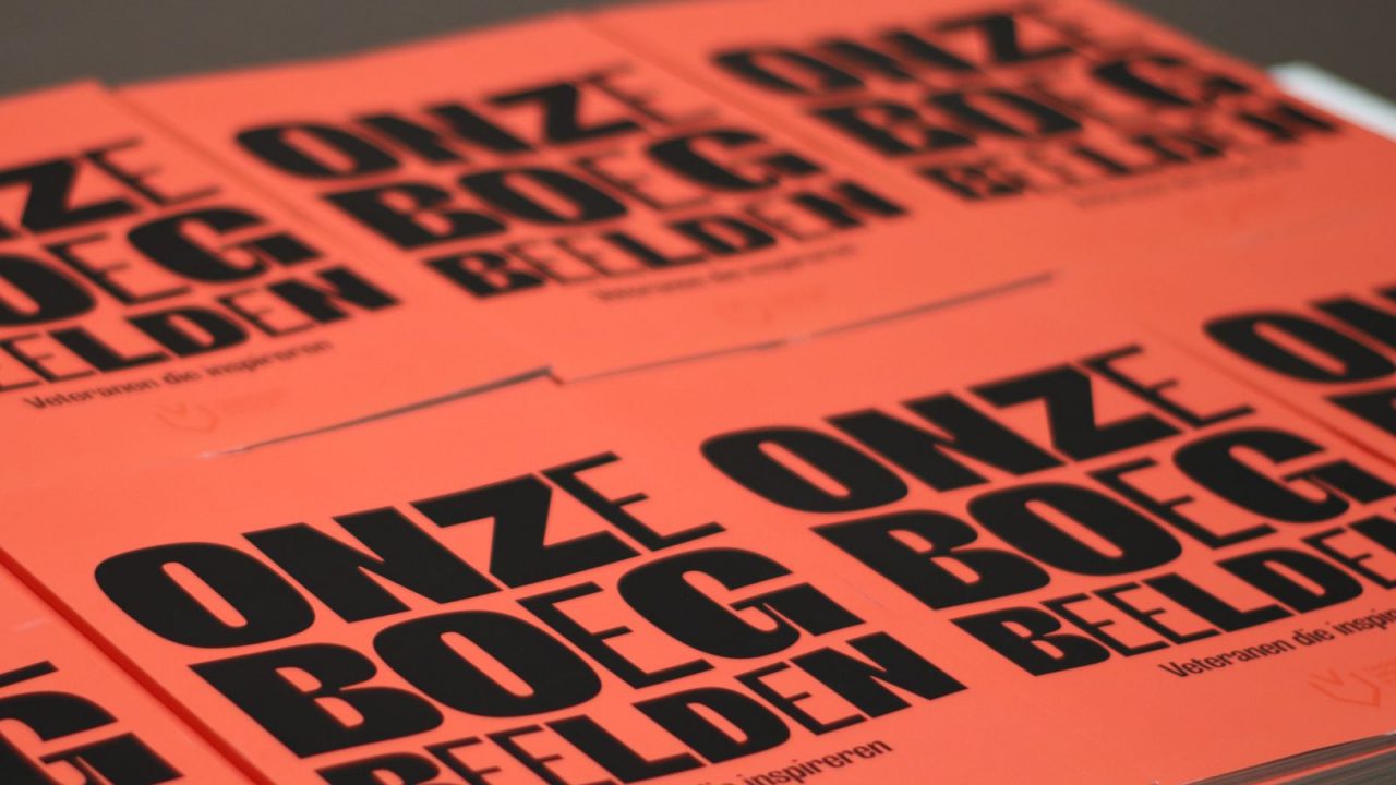 Stapels feloranje magazines met de grote zwarte titel “Onze boegbeelden” liggen naast elkaar uitgestald.