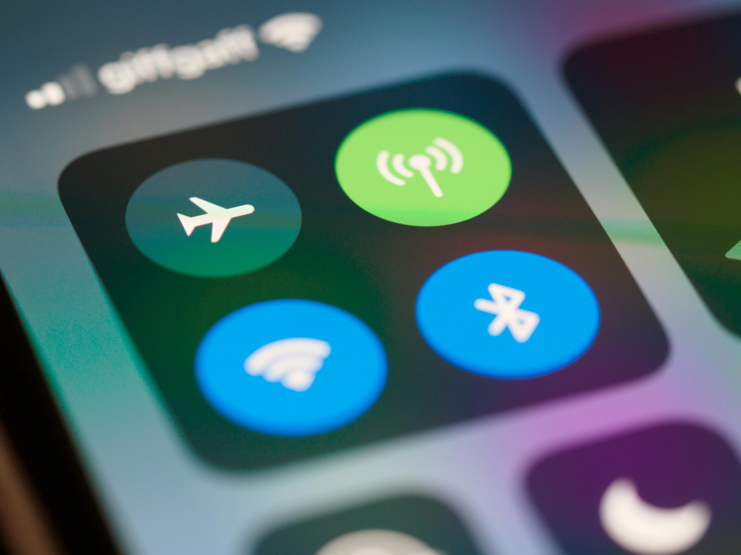 Close-up van het bedieningspaneel op een smartphone met ronde knoppen voor vliegtuigmodus, mobiele data, wifi en bluetooth. De pictogrammen zijn duidelijk zichtbaar tegen een donkere achtergrond met zachte, gekleurde lichtreflecties.