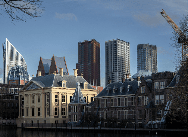 “Uitzicht op Den Haag met historische gebouwen aan de Hofvijver op de voorgrond en moderne hoge kantoortorens in de skyline daarachter, onder een heldere blauwe lucht.