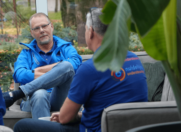 Man in gesprek met andere man met grijs haar. De man met het grijze haar draagt een t-shirt met de tekst 'Nuldelijnsondersteuning'