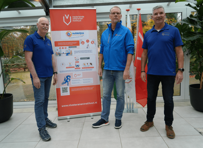 Drie mannen staan voor een banner van het Nederlands Veteraneninstituut en de nuldelijnsondersteuning.