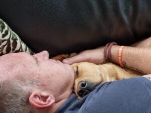 Op de foto ligt Robert van der Holst met zijn assistentiehond in de armen.