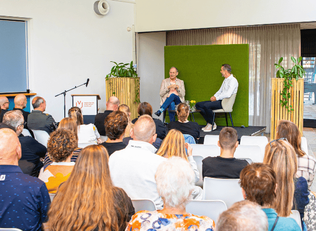 Een volle zaal met op het podium Mart de Kruijf en Marc Pollen die een podcast aan het opnemen zijn.