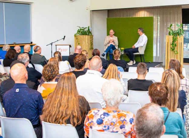 Een volle zaal met op het podium Mart de Kruijf en Marc Pollen die een podcast aan het opnemen zijn.