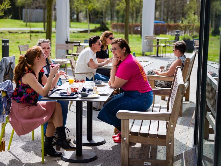 acht vrouwen zitten buiten in de zon aan tafel te lunchen